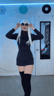 a woman in a black dress and white wig is standing in front of a mirror