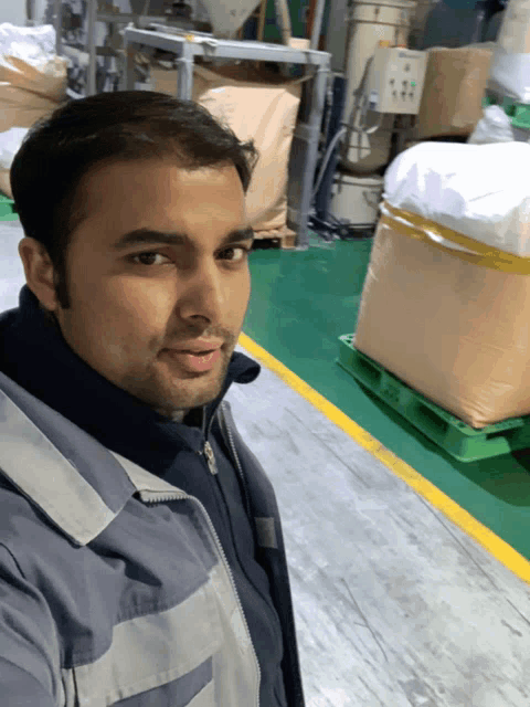 a man in a blue jacket is standing in a warehouse with bags on the floor