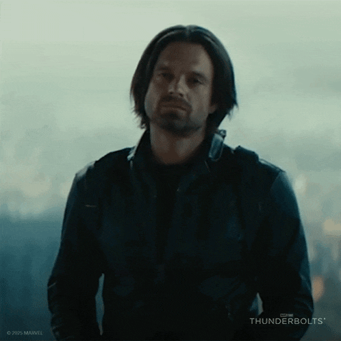 a man with long hair and a beard is wearing a black leather jacket and looking at the camera .