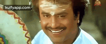 a man with a mustache and a white powder on his forehead is smiling and looking at the camera .