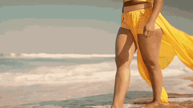 a woman in a yellow top and shorts is walking on the beach