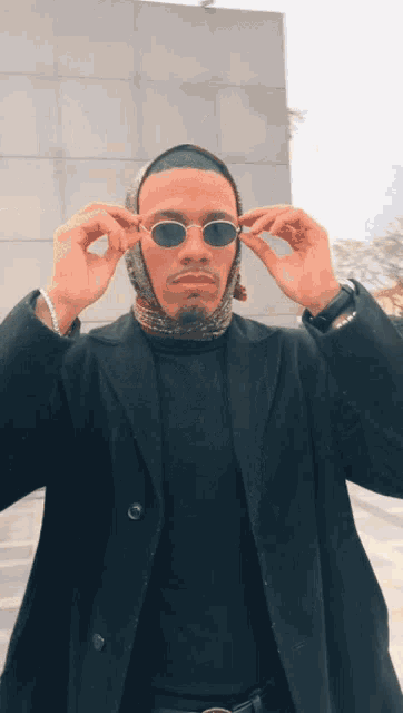 a man wearing sunglasses and a scarf around his head looks at the camera