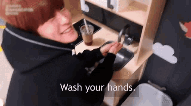 a young boy is washing his hands in a wooden kitchen sink .