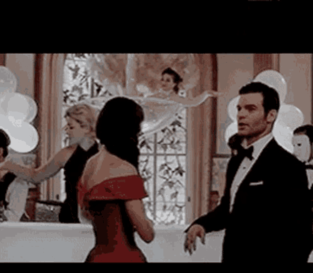 a man in a tuxedo and a woman in a red dress are dancing in a room with balloons .
