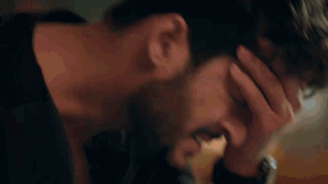 a man with a beard is holding his head in his hands .