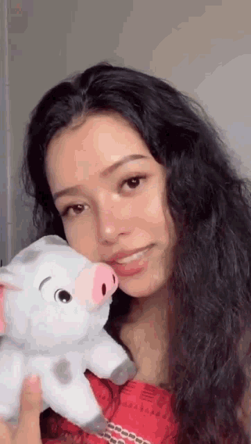 a woman is holding a stuffed pig in her arms and smiling .