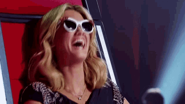 a woman wearing sunglasses is sitting in a chair laughing .