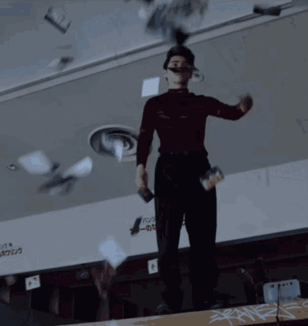 a man in a red sweater is standing on a table with papers falling around him