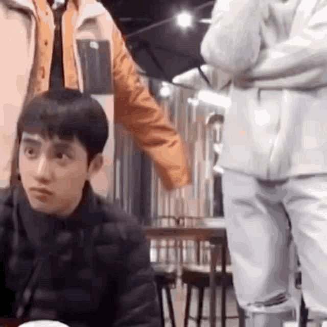 a man is sitting at a table in a restaurant with a group of people standing around him .