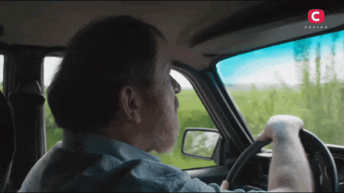 a man is driving a car with a c on the bottom right