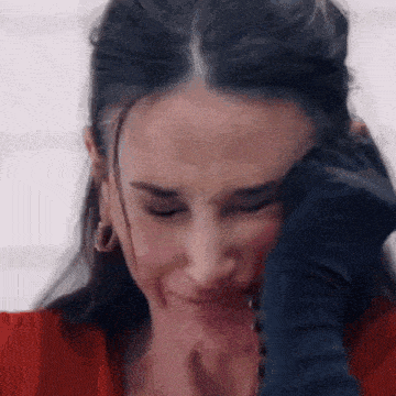 a woman in a red shirt is covering her face with a black glove