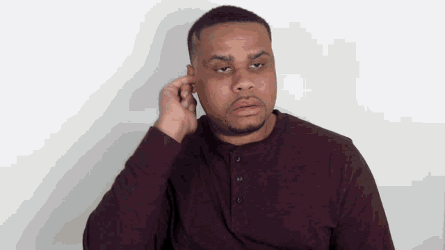 a man in a maroon shirt is covering his ears with his hand
