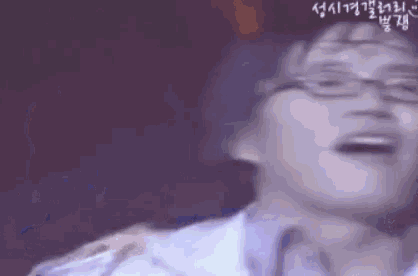 a man wearing glasses is laughing with his mouth open while holding a microphone .