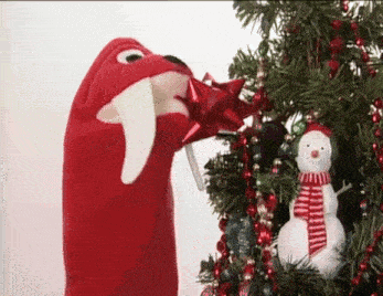a red puppet is decorating a christmas tree with a snowman