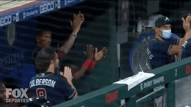 a group of baseball players applaud in a dugout sponsored by geico and fox deportes
