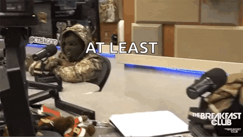 a person in a mask is sitting in front of a microphone with the words at least written on the bottom