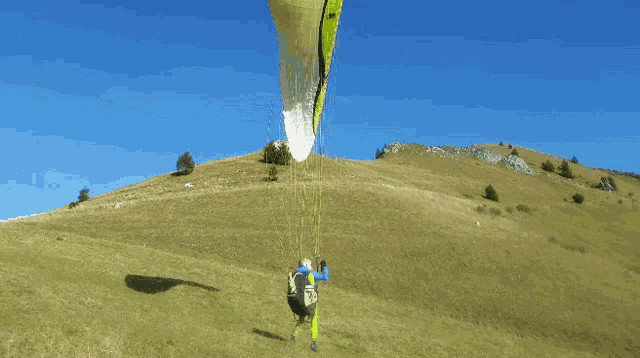 a person flying a parachute over a grassy hillside