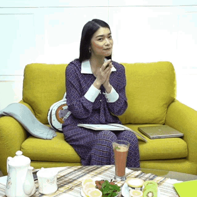 a woman is sitting on a yellow couch with her hands folded in front of her face