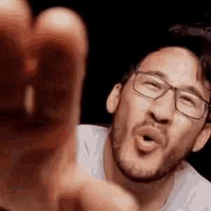 a man with a beard and glasses is pointing at the camera with his finger .