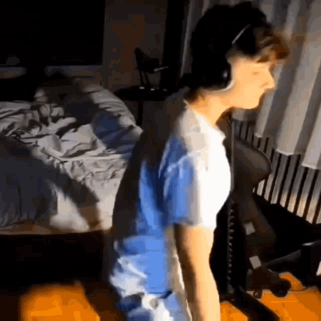 a man wearing headphones is standing in front of a bed in a room .