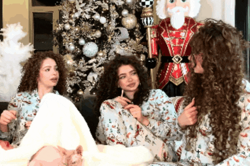 three women are sitting in front of a christmas tree and a nutcracker statue