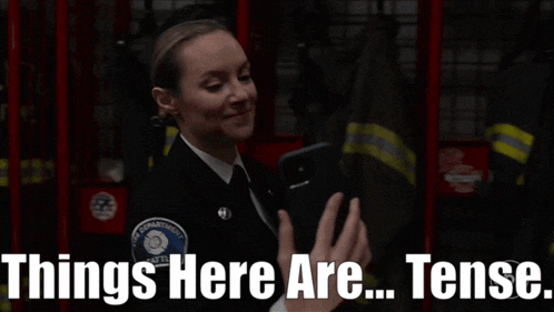 a woman in a fire department uniform is holding a cell phone with the words things here are tense below her