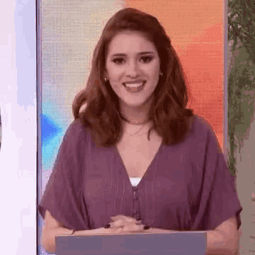 a woman in a purple top is smiling while standing in front of a laptop computer .