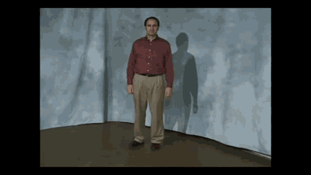 a man in a red shirt and khaki pants is standing in front of a blue wall