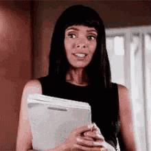 a woman in a black tank top is holding a clipboard and looking at the camera .