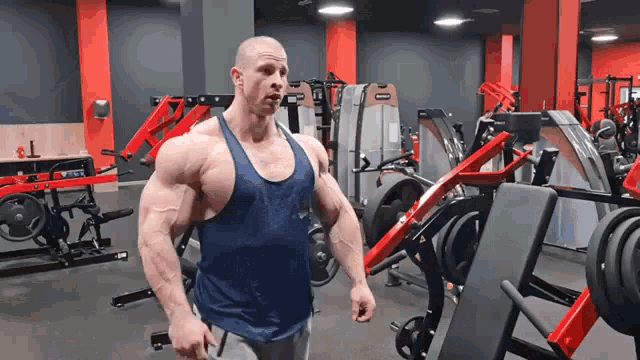 a man in a blue tank top is standing in a gym holding a barbell