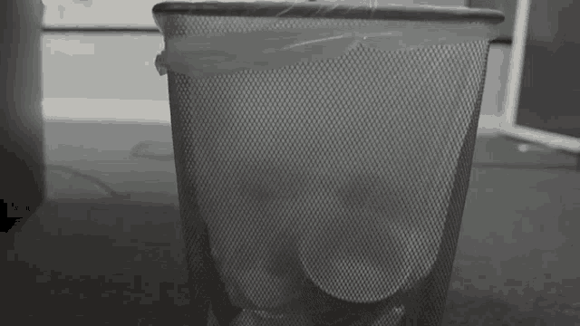 a black and white photo of a trash can filled with papers .