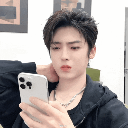 a young man is looking at his cell phone with a necklace around his neck that says ' yummy ' on it