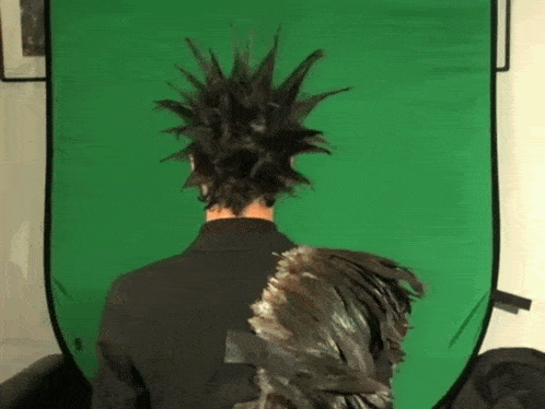 a person with a mohawk and feathers on their back stands in front of a green screen