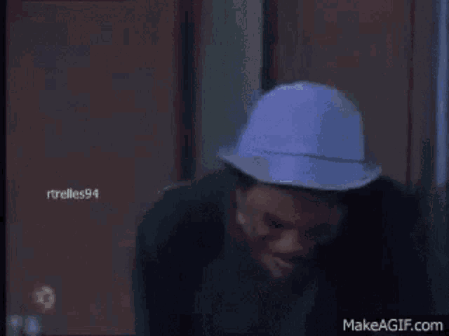 a man wearing a blue hat is sitting on a couch with makeagif.com in the lower right corner