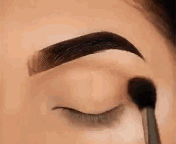 a close up of a woman applying eye shadow to her eyebrows with a brush .