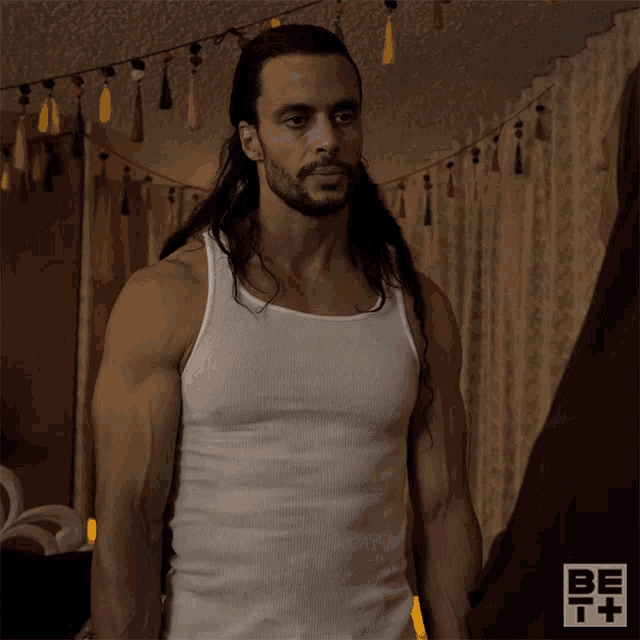 a man with long hair is wearing a white tank top with the letters bet on the bottom
