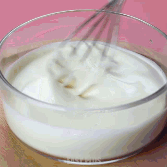 a glass bowl of whipped cream is being whisked by a whisk