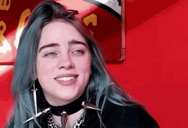 billie eilish is wearing a choker and earrings and smiling .