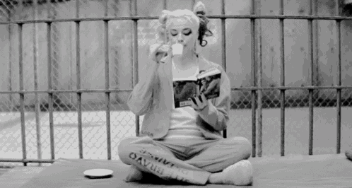 a black and white photo of a woman sitting on the ground reading a book .