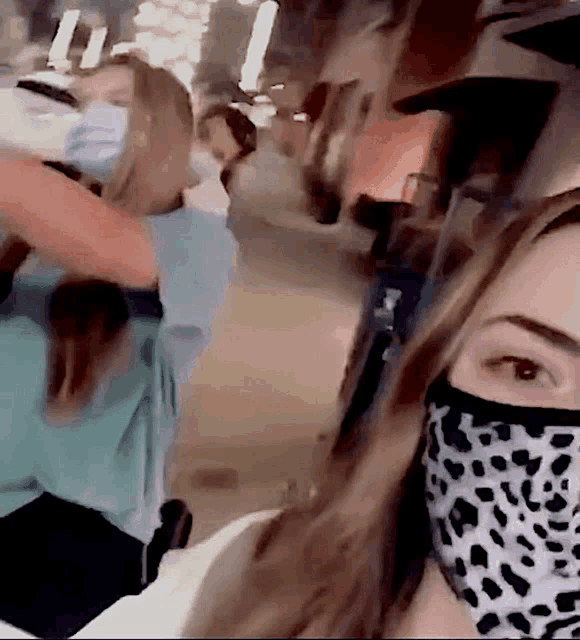 a woman wearing a leopard print face mask is standing next to another woman wearing a mask