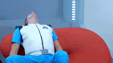 a man laying on a red couch wearing a white vest with the letter a on it