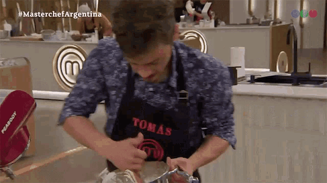 a man wearing an apron that says tomas on it is mixing something in a bowl