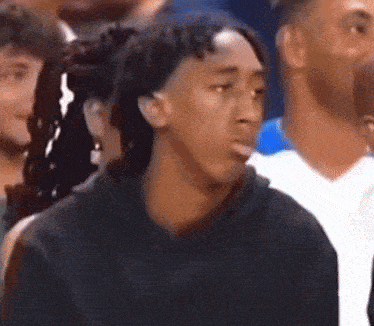 a young man is sitting in a crowd of people making a funny face .