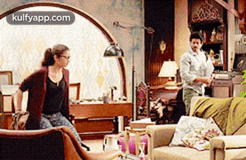 a woman is sitting on a couch in a living room while a man stands in the background .