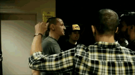 a man in a plaid shirt is hugging another man in a black and yellow hat .