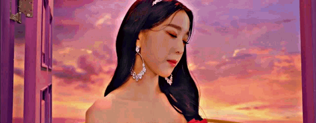 a woman in a red dress and earrings is standing in front of a sunset .