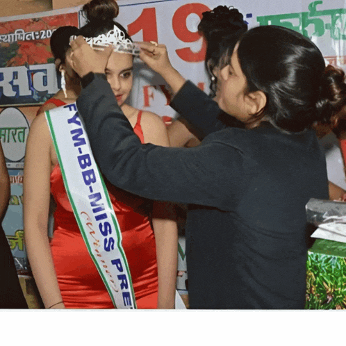 a woman is putting a crown on a woman wearing a sash that says fym-bb-miss pre