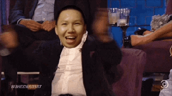 a man in a suit is sitting on a couch with his arms outstretched and laughing .