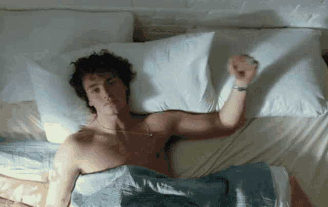 a shirtless man is laying on a bed with his arm up