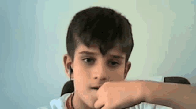 a young boy wearing ear buds is sitting in a chair and covering his mouth with his hand .